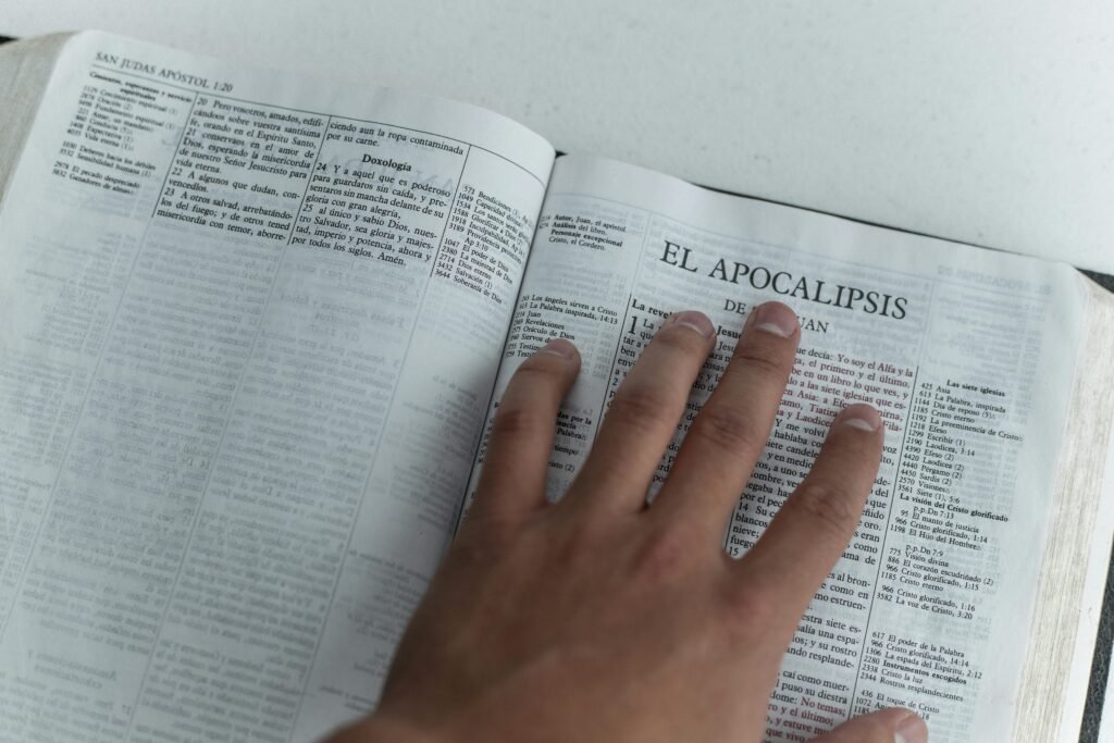 A hand touching Bible pages open to the Book of Revelation, symbolizing faith and study.