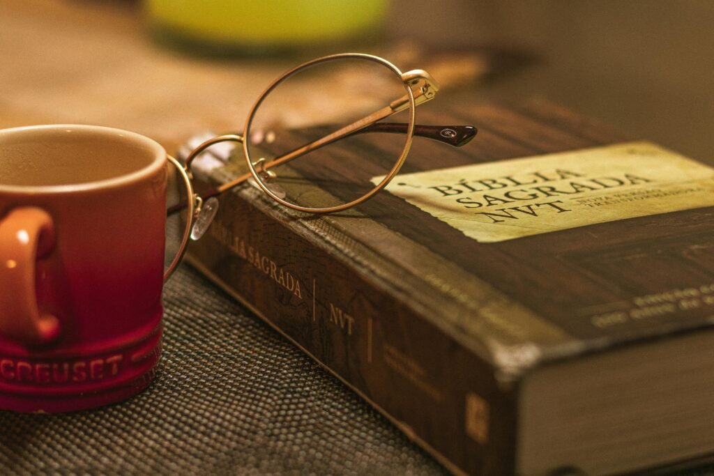 A Biblia Sagrada with glasses rests on a table beside a red mug, symbolizing relaxation and reflection.