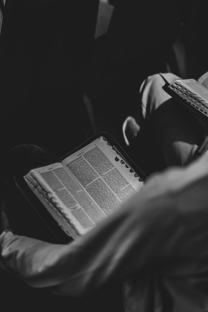 Black and white photo of a person reading an open Bible, focused on the book.